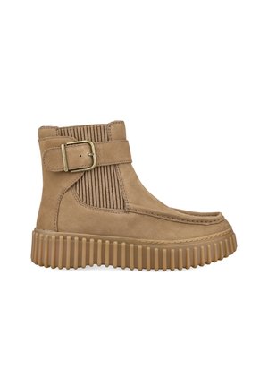 Tan suede ankle boot with thick ridged sole, side buckle strap, and ribbed elastic panel for fit, shown in profile on white background.