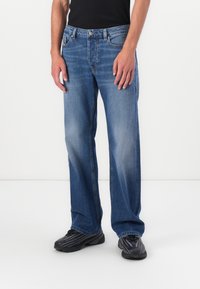 Lichtblauwe denim jeans met een rechte pasvorm, vervaagd aan de voorkant en vijf zakken. Knopen- en ritssluiting, gedragen met zwarte sportschoenen.