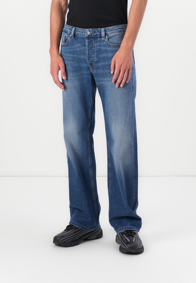 Lichtblauwe denim jeans met een rechte pasvorm, vervaagd aan de voorkant en vijf zakken. Knopen- en ritssluiting, gedragen met zwarte sportschoenen.