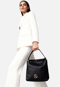 Borsa a mano in pelle nera dalla forma strutturata, con un dettaglio logo dorato e chiusura superiore con cerniera. Il manico è robusto e contrasta bene con il materiale.