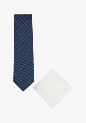 Cravate bleue texturée et pochette blanche soigneusement pliée présentées sur fond blanc.