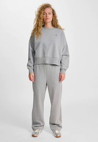 Felpa grigia corta abbinata a pantaloni della tuta grigi larghi. Il tessuto sembra morbido con una texture liscia, caratterizzato da un piccolo dettaglio con logo.