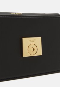 Black leather handbag featuring a gold-tone rectangular clasp with circular detail and brand logo embossed on the front. Textured finish.