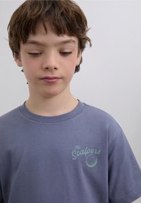 Graues Baumwoll-T-Shirt mit rundem Ausschnitt, kurzen Ärmeln und einem kleinen grünen Logo mit der Aufschrift "The Scalpers" und einem Golfball-Motiv.