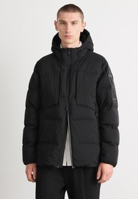 Jachetă puffer neagră cu glugă, închidere cu fermoar și două buzunare frontale. Prezintă o textură netedă și un design minimalist cu un accent logo.