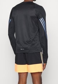 Camiseta deportiva de manga larga negra con un patrón texturizado, acentos de tres rayas azules en las mangas y un logo de "AEROREADY" en el dobladillo.