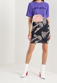 Fialová krátká trička s textem "COULEURS", spárovaná s vypasovanou námořnickou sukní s bílým a béžovým abstraktním vzorem, černou prošívanou ledvinkou a bílými botami s červenými podpatky.