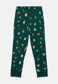 Leggings de pijama verdes com padrões festivos, incluindo árvores, flocos de neve, bastões de doce, biscoitos de gengibre e tambores; material de algodão suave.