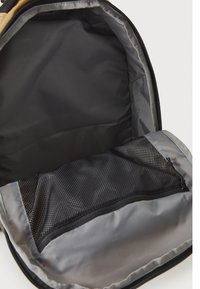 Backpack interior featuring a sleek, dark fabric lining with a large, open compartment and a black mesh zippered pocket for organization.