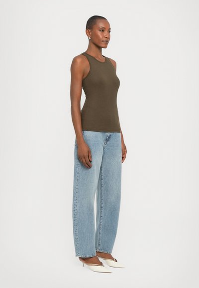 Olijfgroene geribbelde tanktop met een slim-fit ontwerp, gecombineerd met lichtblauwe high-waisted jeans en witte puntige hakschoenen.