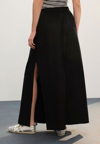 Crna duga suknja s prorezom na lijevoj strani, elastičnim pojasom i laganim materijalom. Uparena sa srebrnim sportskim tenisicama.