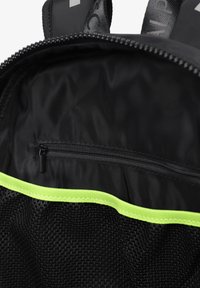 Interior de mochila negra con un bolsillo de malla y un compartimento con cremallera. Presenta un borde de acento verde brillante a lo largo del borde superior. Textura suave.