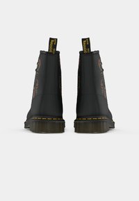 Stivali neri con ricami floreali colorati, cuciture gialle attorno alla suola e linguette nere con la scritta "WITH SOLES Bouncing" viste dal retro.