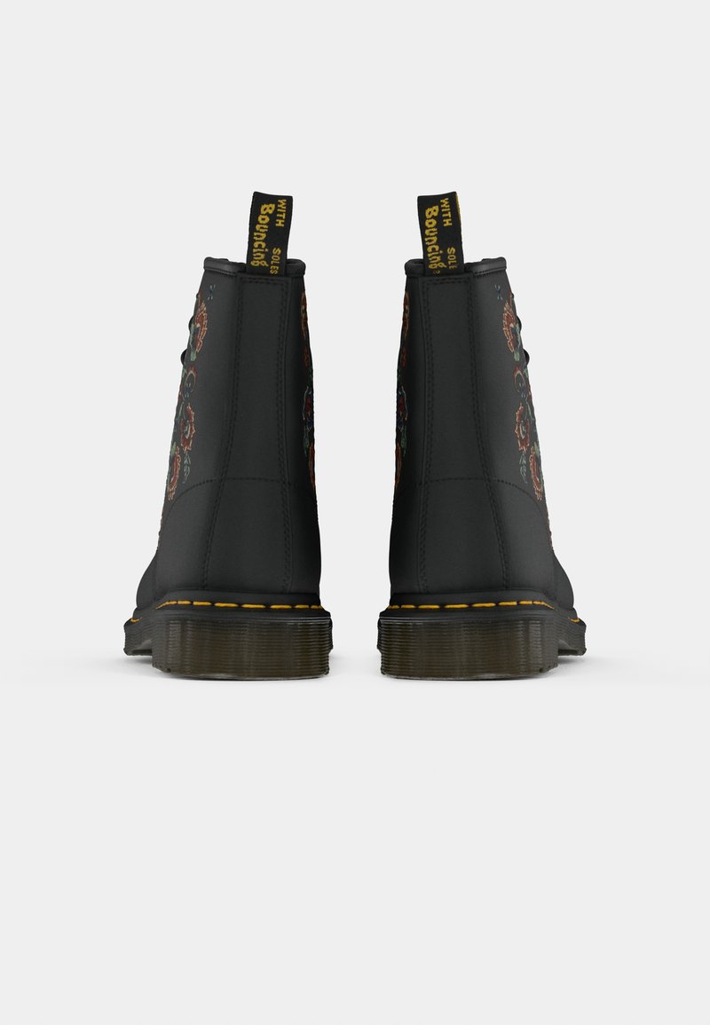 Bottes noires avec une broderie florale colorée, surpiqûres jaunes autour de la semelle et languettes noires avec l'inscription "WITH SOLES Bouncing", vues de l'arrière.