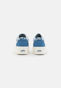 Blue canvas sneakers with a white rubber sole. Features patterned accents on the heel and a rounded design. Branding visible on the back.