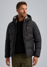 Bunda typu puffer v tmavo sivej farbe s textúrovaným povrchom, s kapucňou, zipsovými vreckami a jemným kožušinovým podšívkou pri golieri.