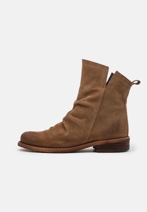 Bottine en daim marron avec texture perforée, tige décontractée, semelle en bois et languette de traction à l'arrière, vue de profil sur fond blanc.
