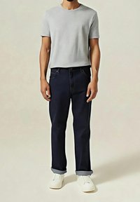 Camiseta gris de manga corta, vaqueros azul oscuro con bajos remangados y zapatos blancos sin cordones. Diseño sencillo, textura suave y corte clásico.