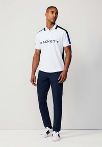 Bílá polo košile s námořnickými akcenty, s logem "HACKETT". V kombinaci s námořnickými kalhotami a bílými teniskami. Hladká textura, klasický střih.