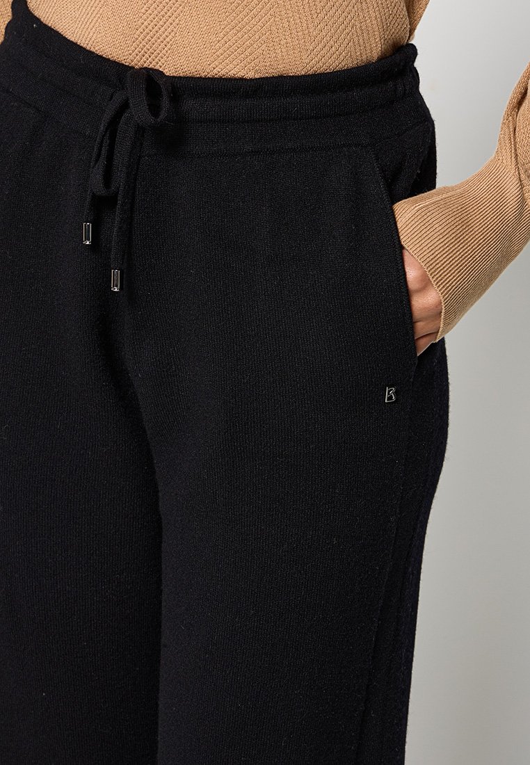 Schwarze gestrickte Lounge-Hosen mit elastischem Bund und Kordelzug, ausgestattet mit Seitentaschen und einem kleinen Logo in der Hüfthöhe. Weiche Textur.