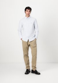 Lysblå stribet skjorte med lange ærmer og et lille logo, parret med beige chinos og sorte loafers. Simpelt design, glat tekstur.