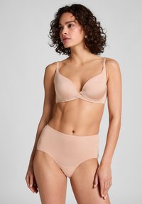 Nude Dessous-Set mit einem leicht gepolsterten BH mit gekreuztem Design und hoch taillierten Slips. Glatter, nahtloser Stoff mit subtiler Textur.