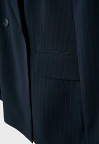 Mørk marineblå blazer med tynde striber, klaffelomme og en enkelt sort knap synlig på venstre side.