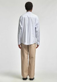 Jasnoniebieska i biała koszula w paski zapinana na guziki z długimi rękawami, zestawiona z kremowymi szerokimi spodniami i czarnymi butami.