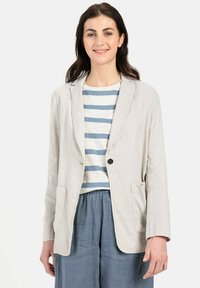 Lichtbeige linnen blazer met notch-kleppen, enkele knoopsluiting en voorzakken, gedragen over een gestreept wit-blauw shirt.