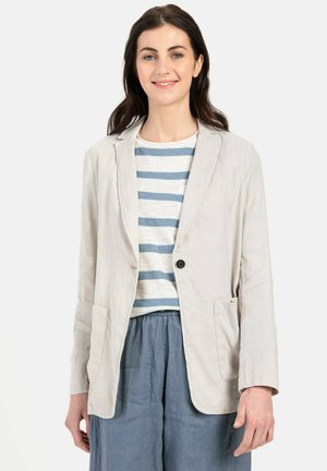 Lichtbeige linnen blazer met notch-kleppen, enkele knoopsluiting en voorzakken, gedragen over een gestreept wit-blauw shirt.