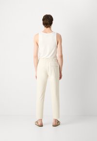 Pantalones beige ligeros con un ajuste relajado, cinturilla elástica y bolsillo trasero, combinados con una camiseta sin mangas blanca entallada y sandalias casuales.