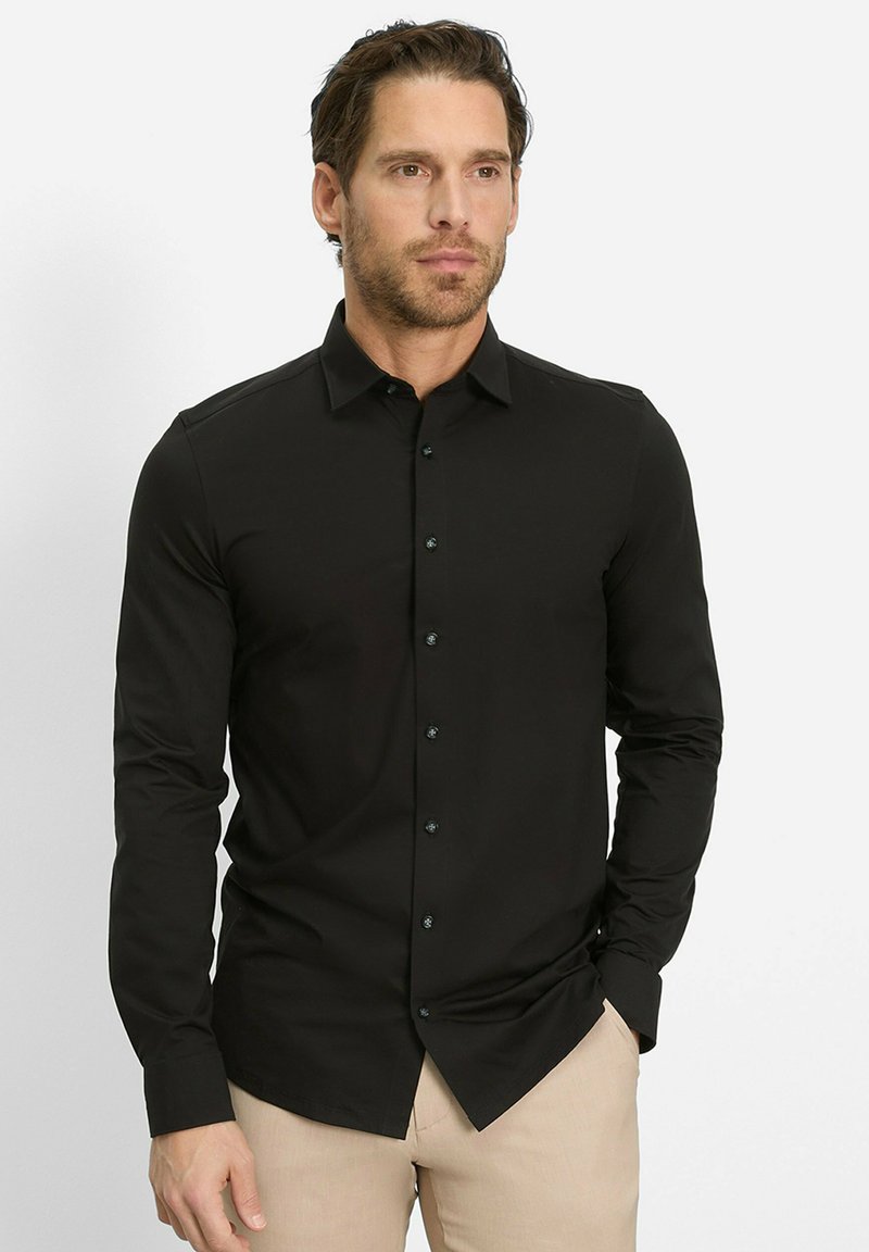 Zwarte lange mouwen knoopshirt met een kraag, voorzien van donkere knopen en een gladde textuur, gedragen met lichtgekleurde broeken.