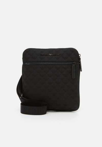 Black quilted crossbody bag featuring a zip closure, embossed logo, and a flat adjustable strap. Made from durable synthetic material.
