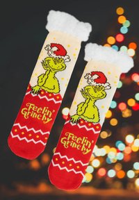 Calzini rossi e crema con un Grinch verde che indossa un cappello di Babbo Natale, polsini bianchi e soffici, e la scritta festiva "Mi sento Grinchy", con motivi a zigzag.