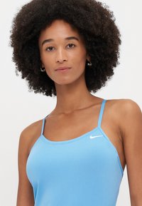Top deportivo de color azul claro, confeccionado en una tela suave. Presenta tirantes finos y un pequeño logo blanco de Nike en la parte superior izquierda.