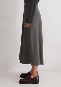 Grå midi-skjørt i et mykt, teksturert stoff med en flytende silhuett, kombinert med mørk burgunder slip-on sko med en liten plattform.