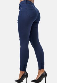 Jeans ajustados de color azul marino con cintura alta, dobladillo desgastado y un ligero desvanecimiento. El material es elástico, diseñado para un ajuste ceñido.