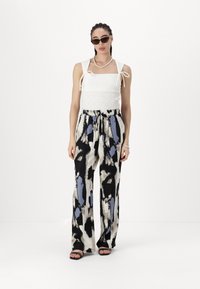 White smocked crop top with ties, paired with black and cream wide-leg pants featuring an abstract blue and black pattern. Black sandals.