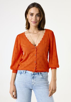 Rode gebreide cardigan met een gegolfde halslijn en driekwart pofmouwen. Voorzien van knopen aan de voorkant en een gestructureerd patroon door het geheel.