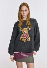 Ciemnoszary sweter dziany z grafiką misia w czerwono-białej pasiakowanej koszulce. Noszony na różowej bluzce z długim rękawem i spódnicy.