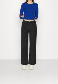 Modrý vysoce střižený top s dlouhým rukávem spárovaný s černými širokými kalhotami s jemným leopardím vzorem, doplněn�ý bílými teniskami.