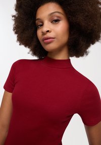 Abito rosso a coste con maniche corte e collo alto. Tessuto liscio con silhouette aderente, che mette in risalto un design attillato.