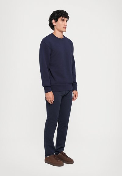 Felpa navy con polsini e orlo a costine, abbinata a pantaloni navy a sigaretta e sneakers in suede marroni. Tessuto morbido, design casual.