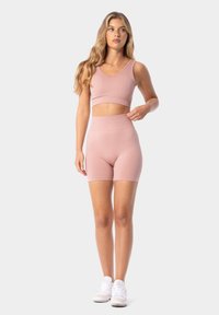 Světle růžový sportovní crop top a odpovídající šortky s vysokým pasem, vyrobené z elastického materiálu, s bezšvovým designem a hladkou texturou.