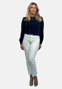 Granatowa bluzka z długim rękawem i dekoltem w kształcie łezki, zestawiona z białymi prostymi dżinsami i wzorzystymi szpilkami. Gładki materiał, dopasowany krój.
