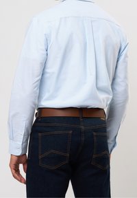 Jasnoniebieska koszula z długim rękawem i mankietami na guziki, zestawiona z ciemnymi dżinsami z pomarańczowym przeszyciem i brązowym skórzanym paskiem. Widok od tyłu.