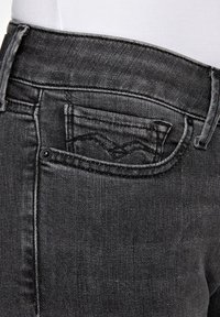 Vaqueros de mezclilla negra con un diseño clásico, un pequeño bolsillo frontal con detalles de costura y una textura suave.