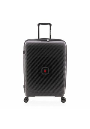 Valise rigide noire avec des rayures diagonales, quatre roues, une poignée extensible et un panneau central rouge avec logo sur fond blanc.