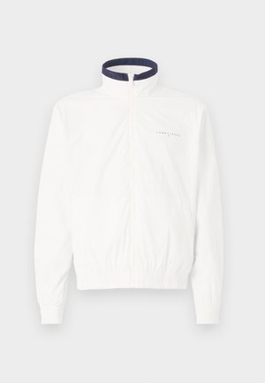 Bijela lagana jakna s mornarskom ovratnikom, prednjim zatvaračem na munju, elastičnim manžetama i pojasom; sadrži suptilni brendiranje na prsima.