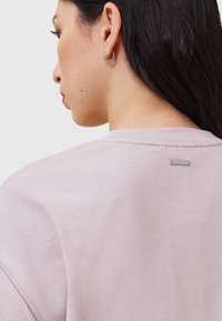 T-shirt di cotone lavanda con collo a giro, caratterizzato da un piccolo etichetta con il marchio sul retro e una texture liscia e morbida.